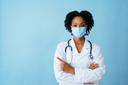 Portrait Of A Doctor In Lab Coat With Face Mask And Arms Crossed Pointing To Side At Copy Space