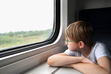 Fototapeta na wymiar Boy looks out train window. Child travels by train. Travel by railway.