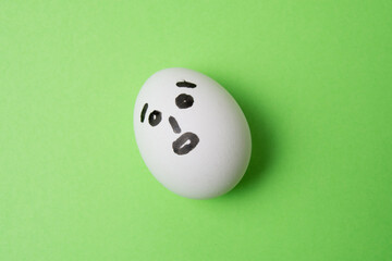 An egg with a surprised face, on a green background with copy space.