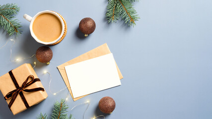 Christmas card mockup, coffee cup, gift box, Xmas decorations, garland, pine branches on blue background. Flat lay, top view. Christmas, New Year, winter holidays concept.