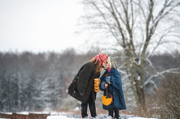 Two beautiful village girls stand on the bench with balalaika and barankas in winter with mum