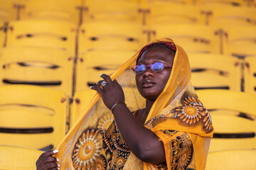 African woman in glasses sitting with patterned yellow suit on an empty audience stand in Accra Ghana west Africa