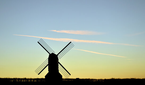 Windmill silhouette at sunset with blue sky and wispy clouds.