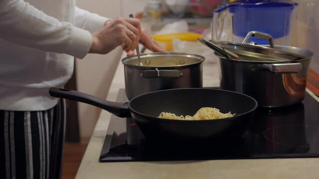 Spaghetti in a pan unrecognizable woman cooking closeup evening kitchen interior
