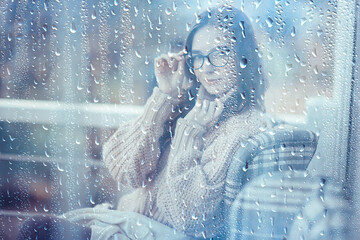 autumn coffee on a rainy day, girl behind a glass with a cup of hot coffee