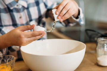 Little girl breaking eggs into a glass bowl preparing a dough. Cute little girl cooking dough in kitchen at home.
