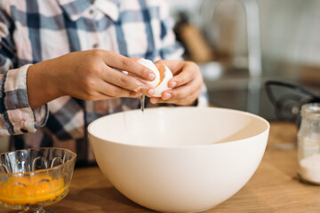 Little girl breaking eggs into a glass bowl preparing a dough. Cute little girl cooking dough in kitchen at home.