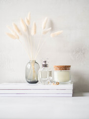 Modern feminine still life of white dry lagurus flower in glass vase, glass scented candle and a...