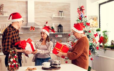 Multigeneration family celebrating christmas with gift boxes wearing red santa hats. Happy loving grandparents celebrating winter holidays and relationship with granddaughter in home with x-mas