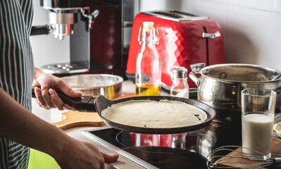 Woman is standing at the stove and frying pancakes in a pan. Concept of the process of making a...