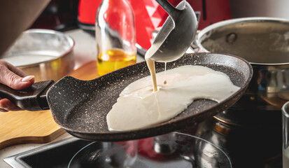 Person pouring the dough into a hot pan and frying homemade pancakes. Concept of making pancakes in your own kitchen
