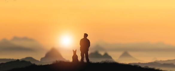 A silhouette of a man with a dog at sunset standing on top of a mountain admiring nature.