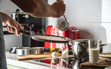 Person pouring the dough into a hot pan and frying homemade pancakes. Concept of making pancakes in your own kitchen