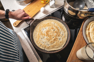 Woman is standing at the stove and frying pancakes in a pan. Concept of the process of making a tasty breakfast at home