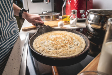 Woman is standing at the stove and frying pancakes in a pan. Concept of the process of making a tasty breakfast at home