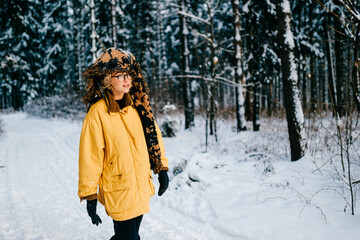 Fototapeta na wymiar Funny strange young hipster girl with glasses and the scarf covering the head walking in the snow forest