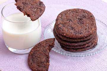 glass of milk and a school chocolate biscuit on a pink background, half biscuit on the glass