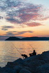 two men fishing on the seashore at sunset