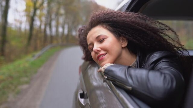 Young afro hair woman travel by car on wild forest autumn road. Female look in opened window from back sit with happy smile