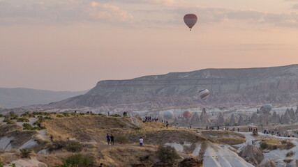People watching a beautiful sunrise with colorful hot air balloons flying in clear morning sky aerial timelapse in Cappadocia, Turkey