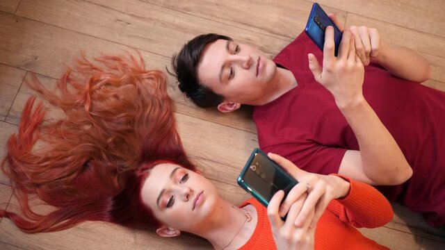 Young Guy and Girl Teenagers use Mobile Smart Phones lying on a Floor