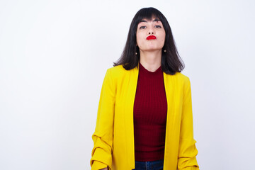 Young beautiful Caucasian woman wearing yellow blazer against white wall keeps palms pressed...