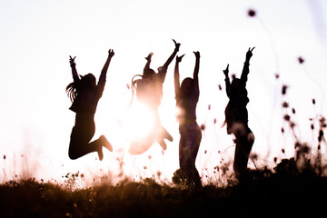 Girls jump together against the sky at top of the mountain.