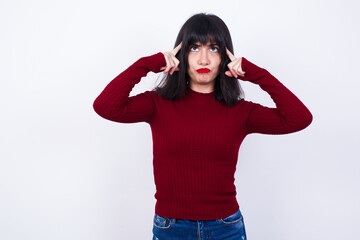 Young beautiful Caucasian woman wearing red T-shirt against white wall, with thoughtful expression, looks away, keeps hand near face, thinks about something pleasant.