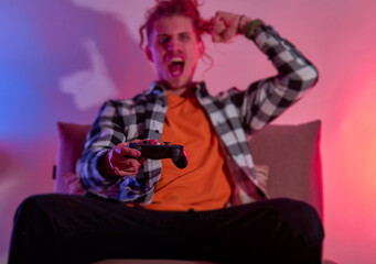 Man holding gamepad controller while playing videogames. Red blue neon light. Close up of man hands playing the video game at home. Face blurry.