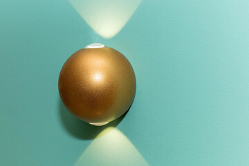 One glowing gold modern metal led lamp on the turquoise color wall. Free space.