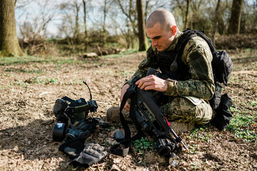 Soldier un Cropat uniform fixing his assault rifle G36 in the forest on a sunny day.