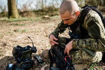 Soldier un Cropat uniform fixing his assault rifle G36 in the forest on a sunny day.