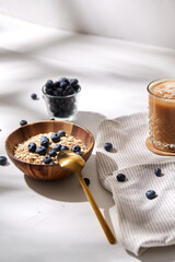food, drinks and breakfast concept - oatmeal in wooden bowl with blueberries and spoon, glass of ice coffee on cork drink coaster and kitchen towel