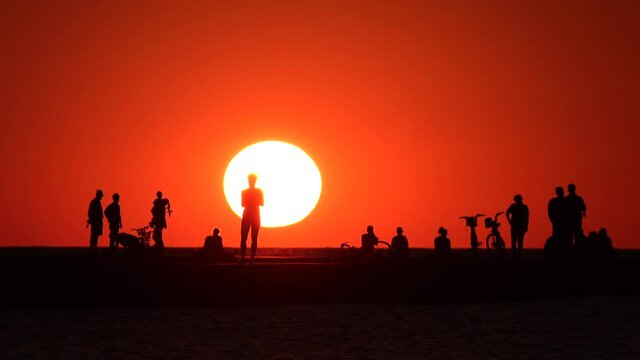 A group of people taking in the sunrise from North Avenue Beach in Chicago with a huge bright sun.