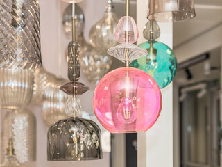 A group of switched-off multicolored lamps with a gray, turquoise, pink glass ceiling is suspended...