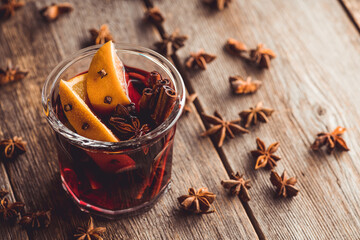 Mulled red wine with oranges and different spices in glass on the rustic background. Christmas...