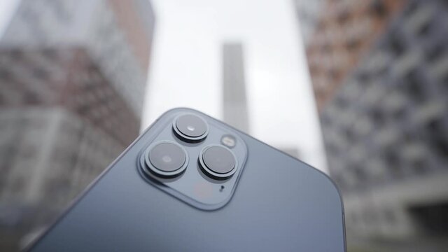 Concept of photography and video shooting. Action. Close up of a super functional camera of high quality on a dark blue smartphone on blurred background of residential high rise buildings.