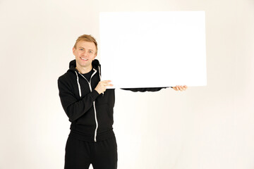 Full length shot of attractive caucasian adult male wearing black training outfit holding blank white sign