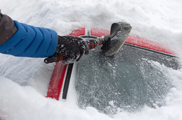 Man clears the windshield of snow on a cloudy winter day