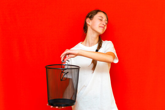 Teenage girl throws glasses in the trash bin.Red studio wall.