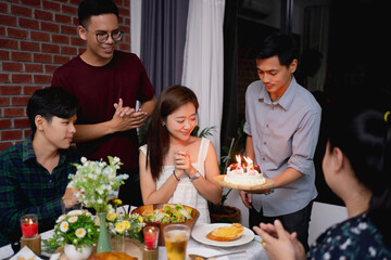 Group of Asian friends were surprised to celebrate their birthday. A man with a birthday cake for his girlfriend to blow the cake