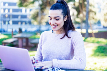 Young beautiful smiling girl sitting in the park using a laptop