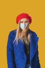 Beautiful woman in a medical mask on a yellow background. Covid-19 coronavirus pandemic concept....