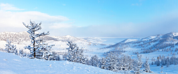 Beautiful landscape of frozen Lake Baikal on a sunny winter day. Panoramic views of the snow-covered Kurkut Bay and tourist wooden houses on the shore from the hill. Winter vacation