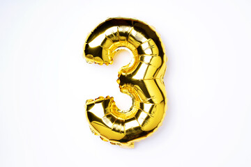 Creative layout. Golden foil balloon number and digit three 3. Birthday greeting card. Anniversary concept. Top view. Copy space. Stylish gold numeral over white background. Numerical digit.