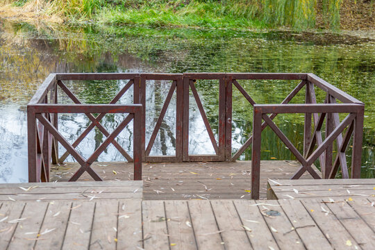 A small wooden pier for boats at the abandoned city pond with duckweed