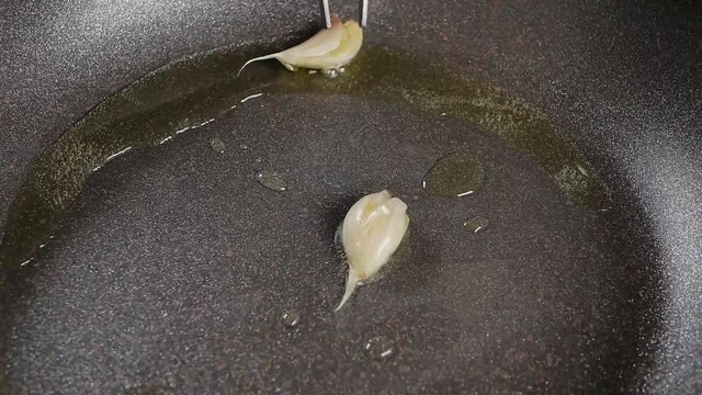 Garlic is turned over with cooking tweezers on a frying pan