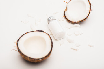 bottle of homemade lotion near coconut halves and flakes on white 
