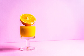 Ein Glas Orangensaft und eine halbierte Orange auf einem isolierten rosa Hintergrund. Gesundes Frühstück, modern.