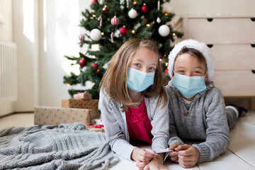 Siblings lying in front of a Christmas tree celebrating Christmas during corona crisis lockdown